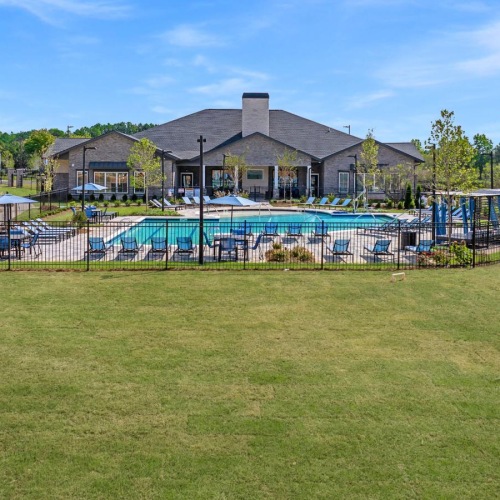 a fenced-in pool area with trees and lounge seating